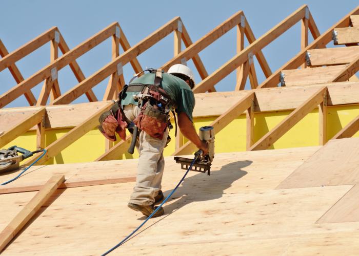 Construction worker using a nail gun to install wooden roofing panels with exposed roof trusses in Cranston