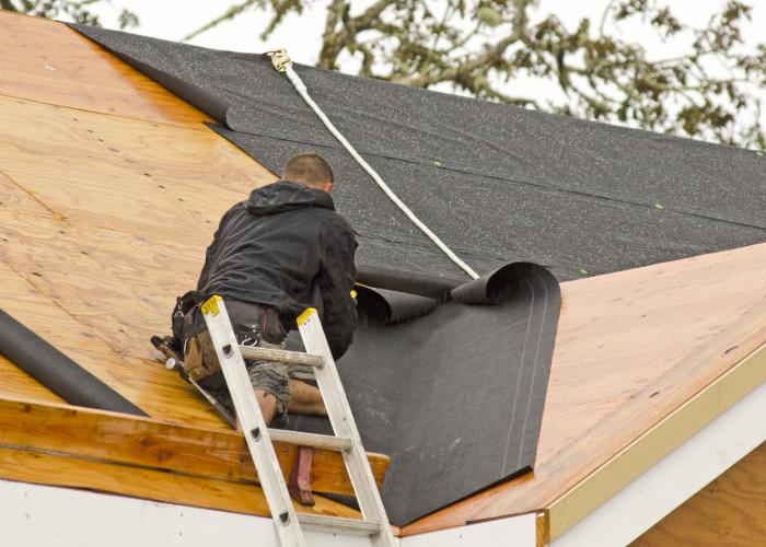 Roofer on a ladder installing black underlayment during a roof repair project in Cranston